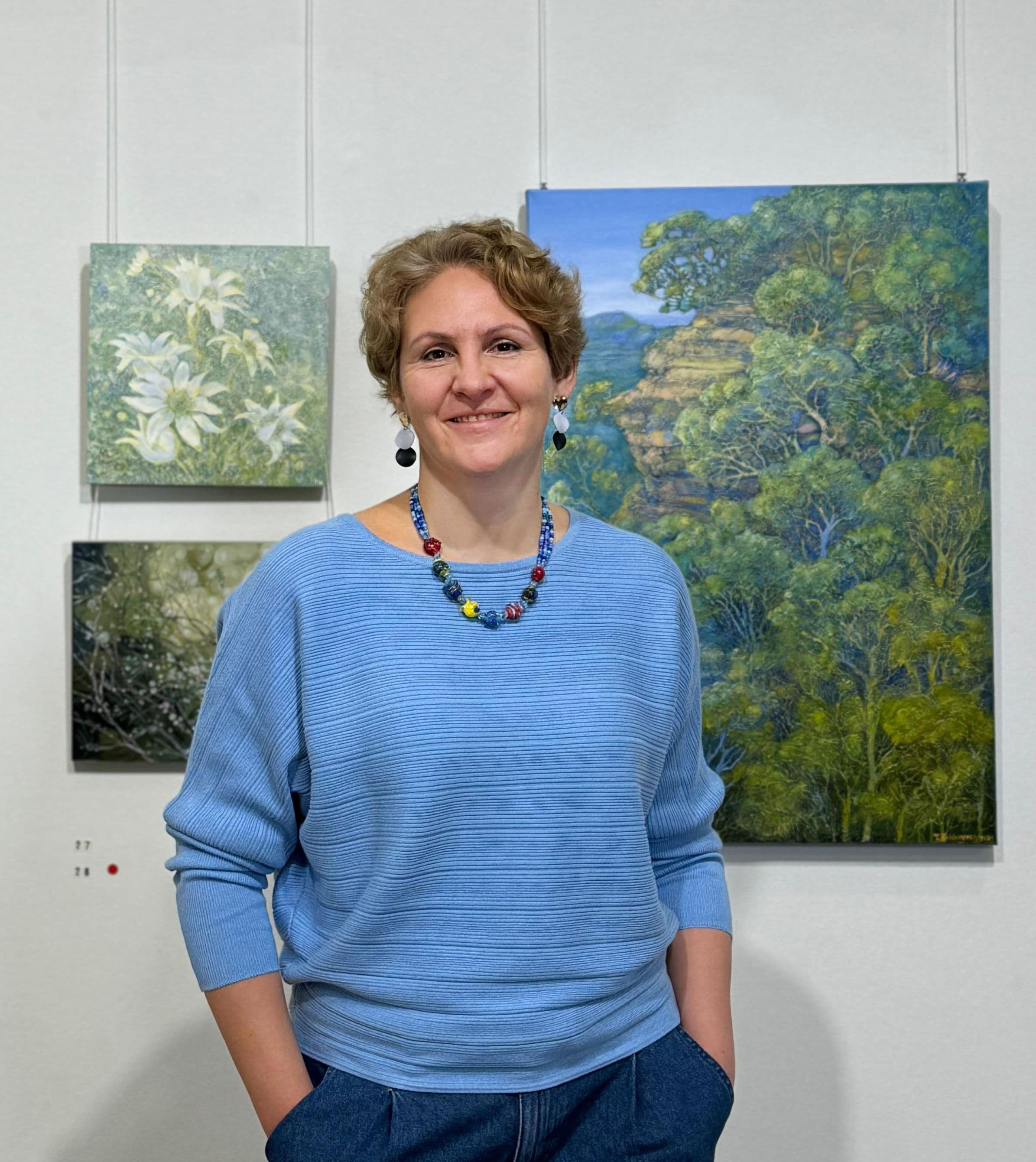 Contemporary artist Tetiana Koldunenko at her art exhibition in Sydney, showcasing realistic Australian landscape paintings.