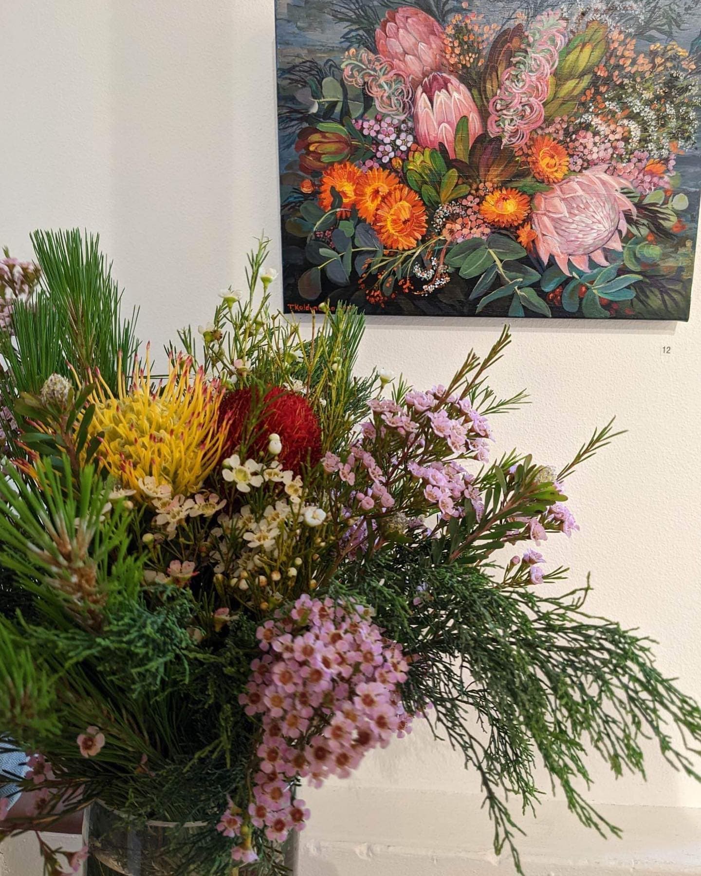 A vase with native flowers in front of painted bouquet of native flowers