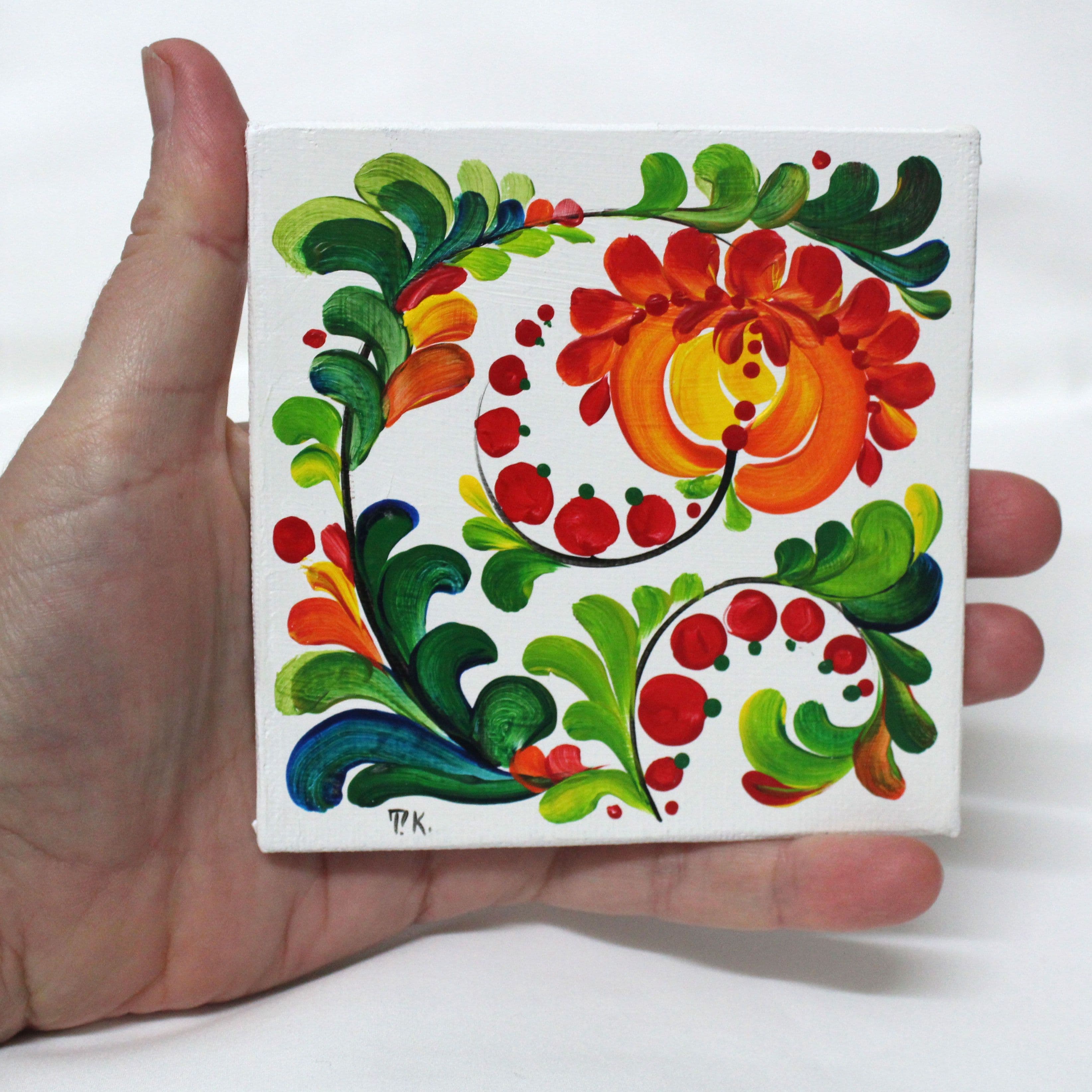 Hand holding a small canvas of Petrykivka flower